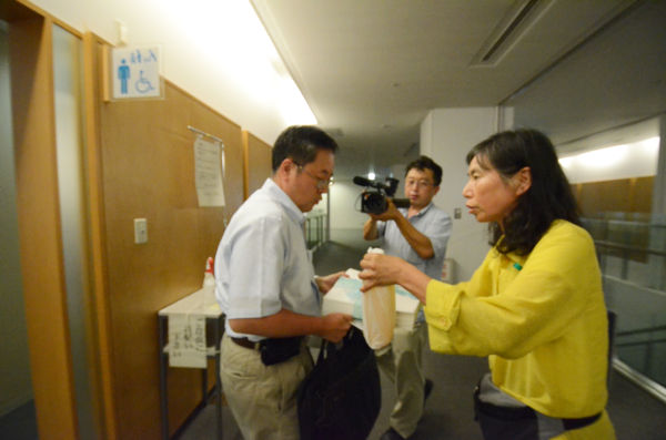 現地対策本部の佐藤室長が署名と尿を持たずに帰ろうとしたため、母親は追いすがり力づくで持たそうとした。（筆者撮影）